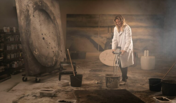 Photo couleur, une femme en blouse blanche dans un atelier d'artiste avec un outil dans les mains